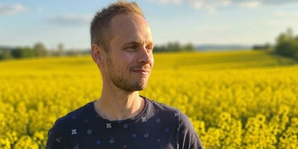 Man står i ett fält av gula blommor under en blå himmel med några moln.