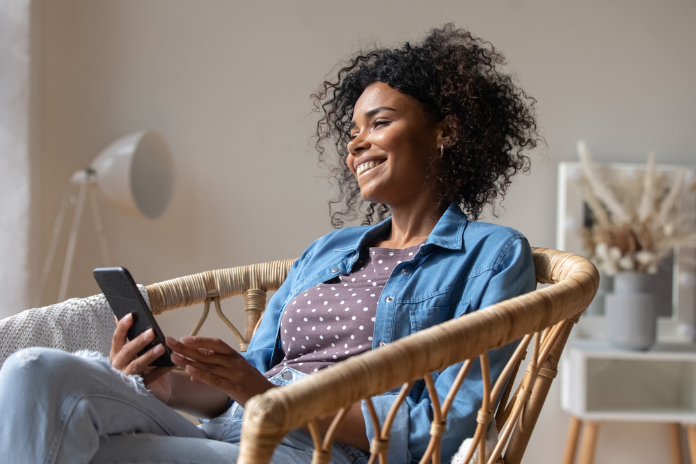 Person sitter avslappnat i en rottingstol och använder en smartphone i ett ljust vardagsrum.