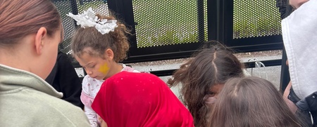 En grupp barn står samlade runt ett bord utomhus, några med färgglada kläder och accessoarer.