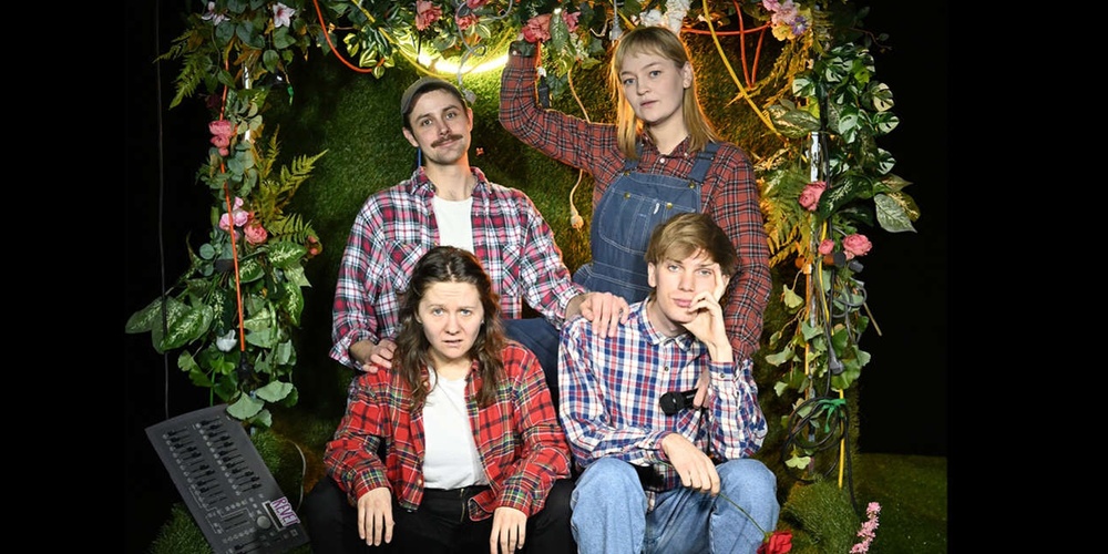 Fyra personer i rutiga skjortor poserar framför en blomsterdekorerad bakgrund, två sitter och två står bakom.