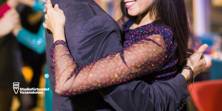 Två personer dansar nära varandra på en social tillställning, leende och festlig stämning.