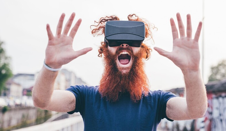En person med rött skägg och hår har på sig ett par VR-glasögon och håller upp händerna framför sig.