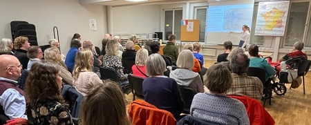 En grupp människor sitter i ett mötesrum och lyssnar på en presentation vid en projektor.