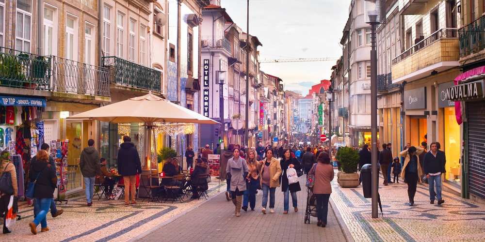 En livlig gågata i en europeisk stad med människor som promenerar och sitter på uteserveringar.