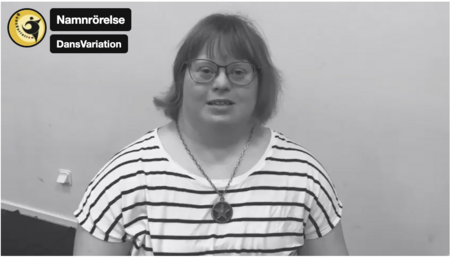 Person med randig tröja och halsband sitter mot en ljus vägg. Två textskyltar syns i övre vänstra hörnet.