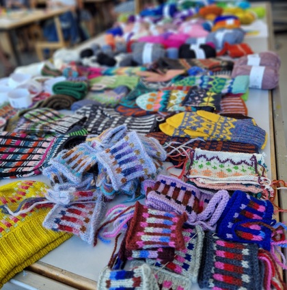 Bord fullt av färgglada stickade vantar, provlappar och garnnystan på en marknad eller workshop.