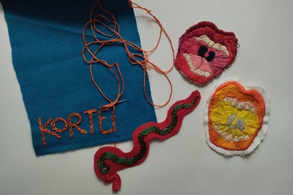 Broderade tygbitar med motiv av munnar, en orm och texten 'KORTEI' på blått tyg.