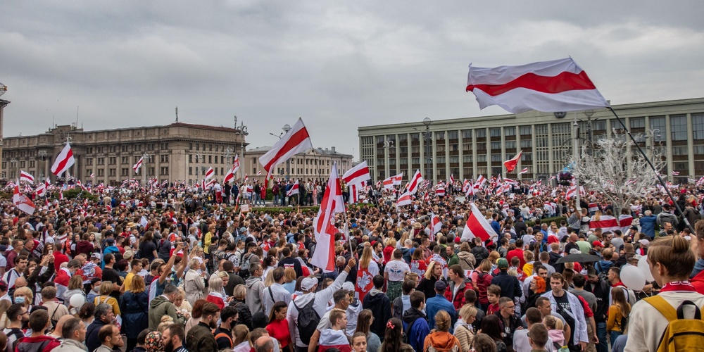 Stor folkmassa samlad på ett torg med många vit-röda flaggor under en demonstration.