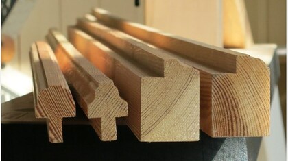 Flera träbalkar med olika profiler ligger staplade på ett bord i ett ljust rum.