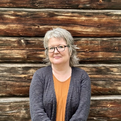 Person står framför en vägg av trästockar med armarna korsade.