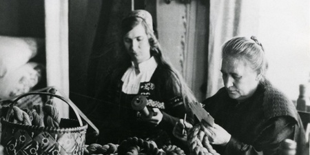 Två kvinnor sitter vid ett bord och arbetar med garn, traditionell miljö, svartvit bild.