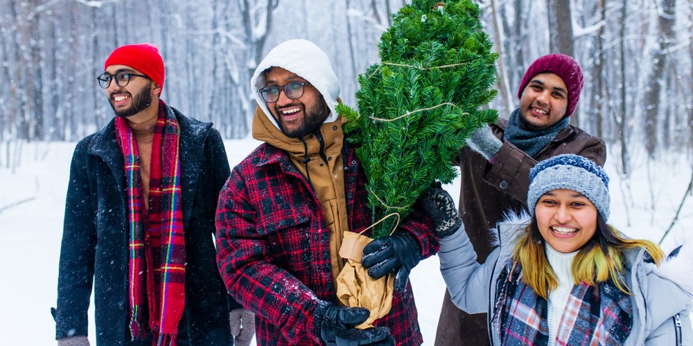 Fyra glada personer bär en julgran i en snöig skog, klädda i vinterkläder.