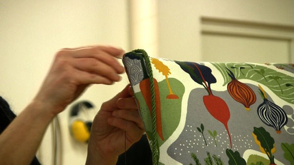 En person syr eller lagar ett kuddfodral med färgglatt grönsaksmönster.