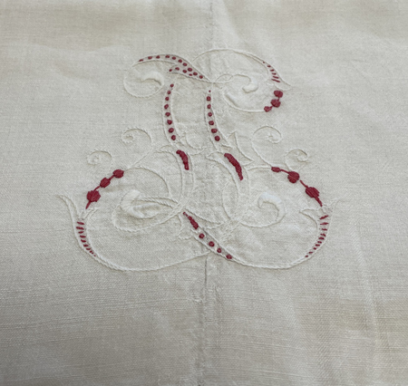 Broderat monogram med vita och röda trådar på vitt tyg, dekorativt och detaljerat mönster.