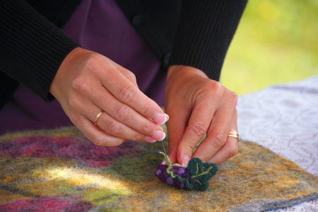 Närbild på händer som arbetar med nåltovning av ull på en filt.