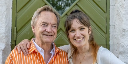 Två personer står nära varandra framför en grön dörr, ena har armen runt den andra.