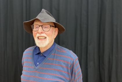 Person med hatt och randig tröja står framför en mörk bakgrund.