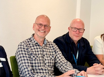 Fyra personer sitter vid ett konferensbord med anteckningsblock, broschyrer och kaffekoppar.