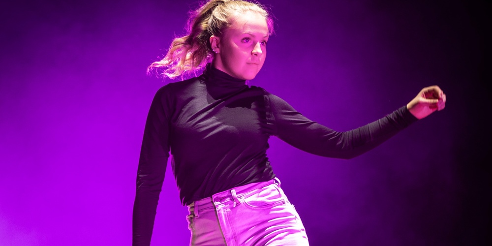 En person dansar barfota på en scen med lila ljus och rökeffekter.