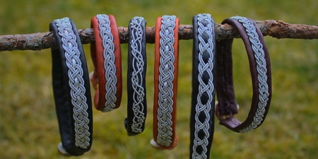 Sex armband med flätade mönster hänger på en gren utomhus med gräs i bakgrunden.