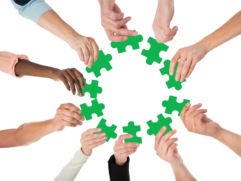 Flera händer håller gröna pusselbitar i en cirkel mot en vit bakgrund.