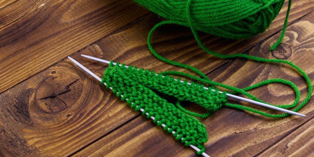 Grönt garnnystan och stickning på träbord med två stickor och påbörjat arbete.