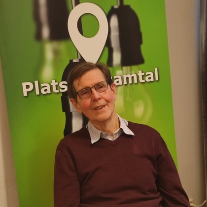 Man med glasögon sitter vid ett bord framför en grön skylt med texten 'Plats för samtal'.