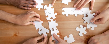 Flera händer samarbetar för att lägga ett pussel på ett trägolv.