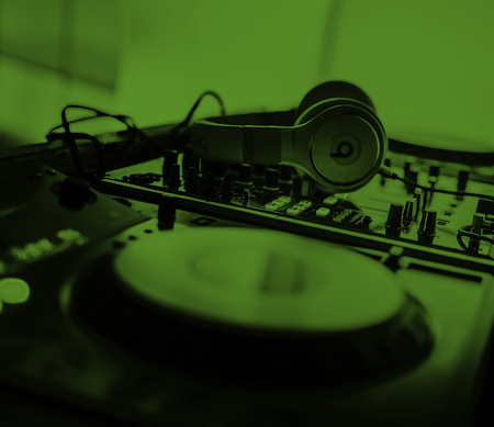 Ett DJ-mixerbord med hörlurar placerade ovanpå, belyst i grönt ljus.