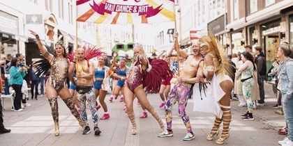 Färgglad dansparad på en stadsgata med utklädda deltagare och publik längs sidorna.