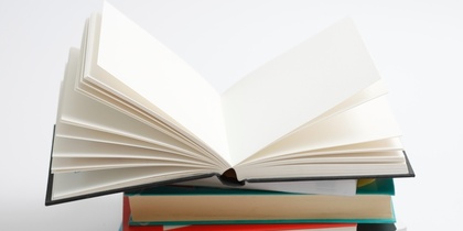 En hög med böcker där den översta boken är uppslagen och resten är stängda, mot vit bakgrund.