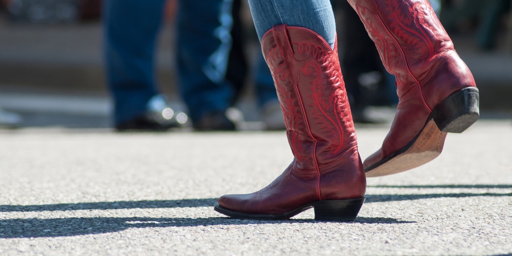 Person i blå jeans och röda cowboyboots dansar utomhus på asfalt.