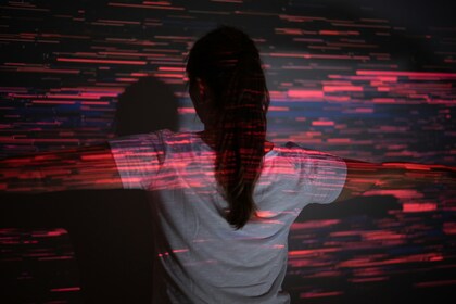 Person med ryggen mot kameran står med utsträckta armar, röda ljuslinjer projiceras på väggen och kroppen.