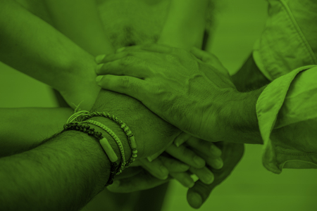 Flera händer lagda ovanpå varandra i en gest av samarbete, bilden har ett grönt färgfilter.