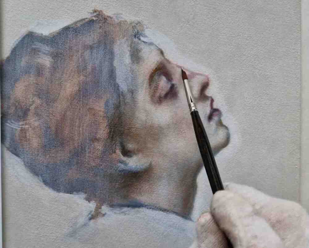 En hand målar ett realistiskt porträtt av en kvinna i profil med en pensel på en duk.