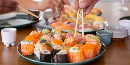 Två personer plockar sushi med ätpinnar från ett fat på ett matbord.
