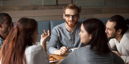 En grupp människor sitter runt ett bord på ett café och samtalar över kaffe och bakverk.
