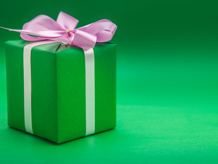 En grön presentask med vitt band och rosa rosett mot en grön bakgrund.
