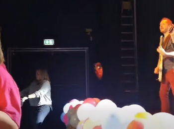 Scenframträdande med musik och dans, ballonger i förgrunden och personer på scen och dansgolv.