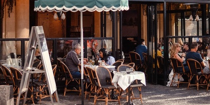 Uteservering på ett parisiskt café med människor som sitter vid bord under en grön markis.