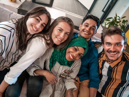 Fem unga vuxna sitter nära varandra i en soffa och ler mot kameran.