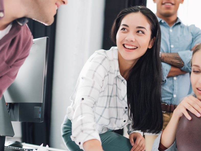 Fyra unga vuxna samarbetar och diskuterar vid ett skrivbord på ett modernt kontor.