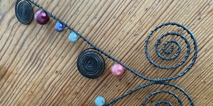 Luffarslöjd dekorativ spiralformad tråd med färgglada pärlor på ett trägolv.