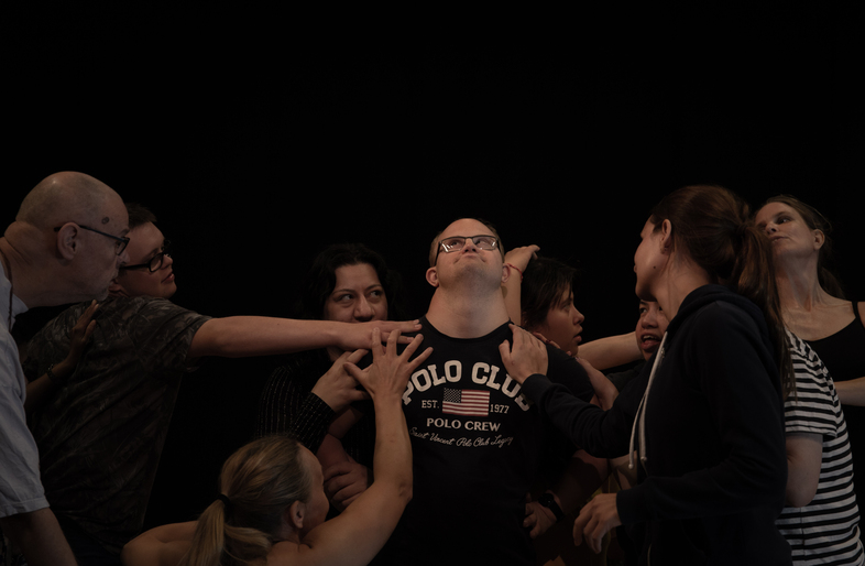 En grupp människor står tätt tillsammans och sträcker ut sina armar mot varandra mot en svart bakgrund.