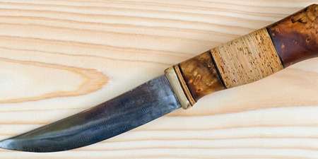 En kniv med trähandtag ligger på en ljus träyta.