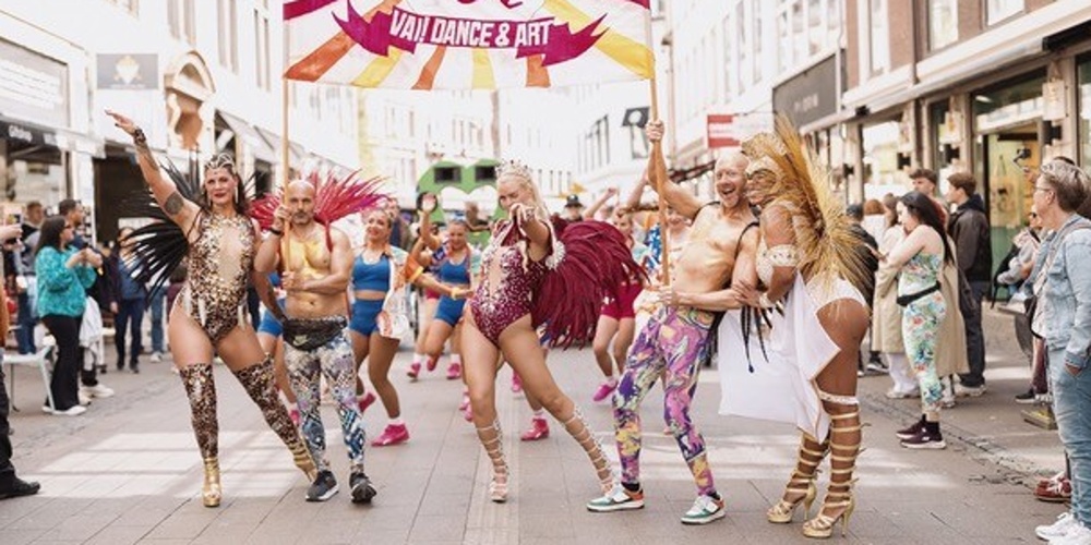 Färgglad dansparad på en stadsgata med utklädda deltagare och publik längs sidorna.