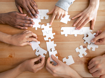 Flera händer samarbetar för att lägga ett pussel på ett trägolv.