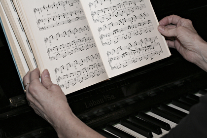En person håller ett nothäfte ovanför ett piano, redo att spela efter noterna.