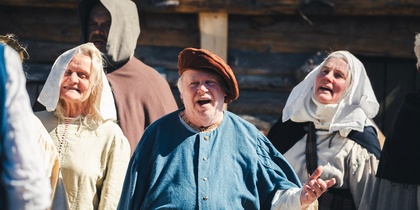 En grupp människor i historiska kläder står utomhus framför en träbyggnad.