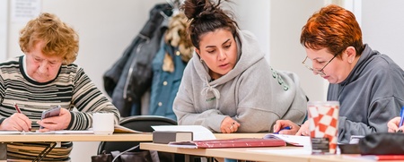 Fyra personer sitter vid ett bord och arbetar tillsammans med papper och pennor i ett klassrum.